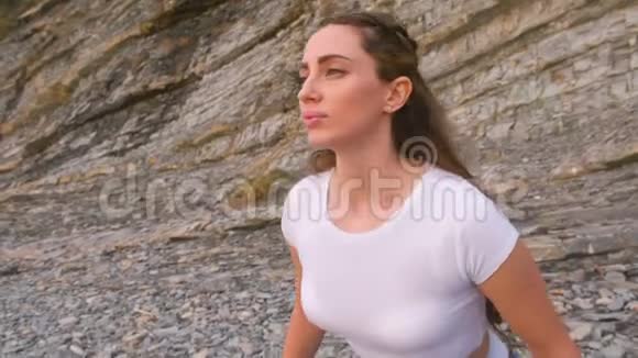 女孩在岩石背景上做呼吸练习时蹲着身体反射面的特写视频的预览图