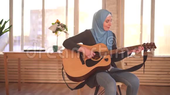 年轻的穆斯林女音乐家在现代公寓里弹吉他视频的预览图