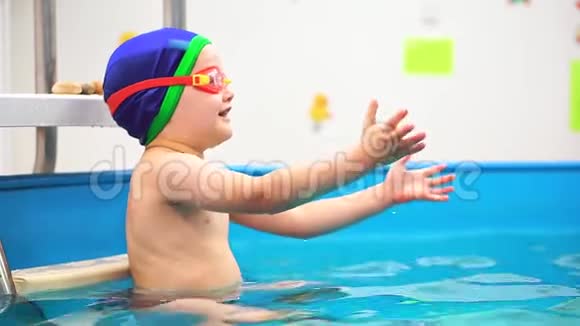 游泳池里的一个小男孩接住了一个蓝色的球他把它扔进泳镜里视频的预览图