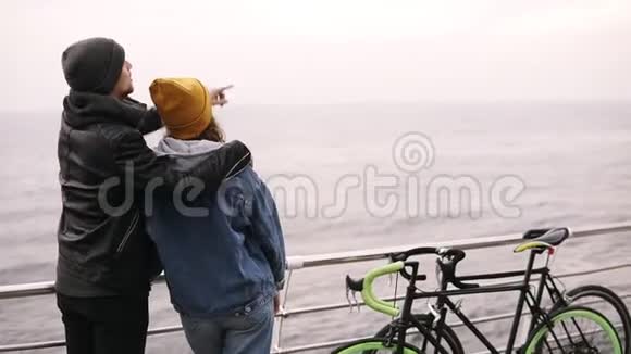 年轻夫妇站在海边的背面肖像爱情夫妇的概念夫妇带自行车夫妇穿暖和的衣服视频的预览图