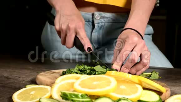雌性手在黄瓜和柠檬切片旁边的切割板上切薄荷叶健康和健康视频的预览图