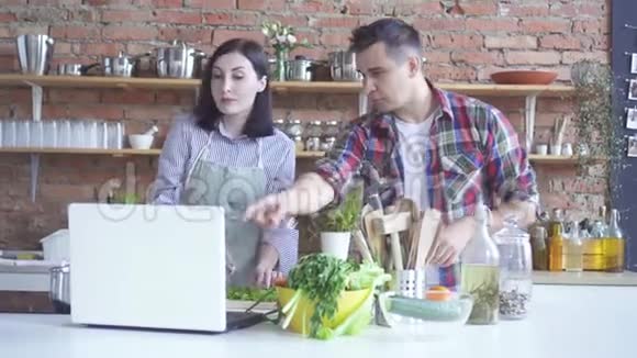 一男一女一家正在厨房里准备一节视频课同时用白色笔记本电脑观看视频的预览图