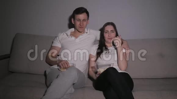 快乐的一对夫妇在电视上看电影坐在家里的沙发上吃爆米花视频的预览图