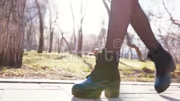 春天美丽的女人穿着黑色的高脚靴和紧身衣在公园里和树木一起走在路上视频的预览图