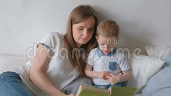 家庭妈妈和她的儿子蹒跚学步的孩子躺在床上看书家庭阅读时间视频的预览图