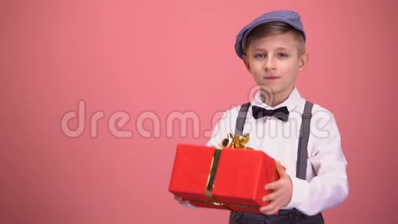 穿着领结和吊带的男孩向相机展示礼品盒节日礼物视频的预览图