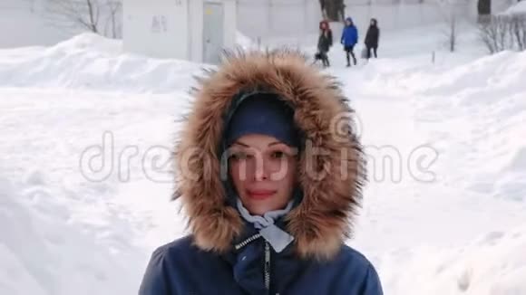特写微笑的女人正在城市的冬季公园里散步白天在下雪的天气里下着雪前线视频的预览图