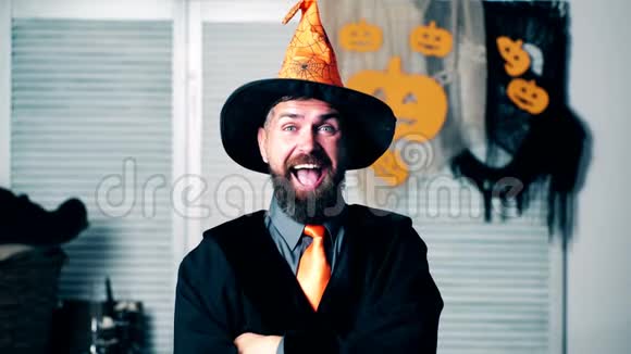 穿着女巫西装的留胡子男人露出了鬼脸一个戴着橙色帽子的长胡子男人在万圣节的节日里做鬼脸视频的预览图