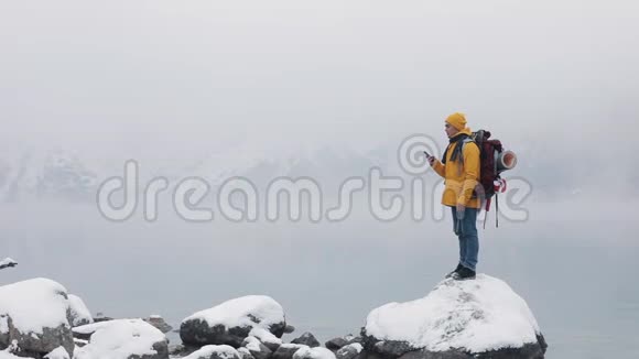 快乐旅行者在徒步冬季旅行中使用智能手机美国徒步旅行者站在山湖附近的石头上白雪公主视频的预览图