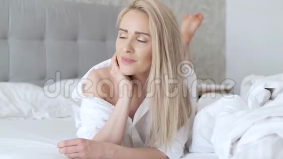 美丽的中年妇女躺在床上穿着白色衬衫微笑着视频的预览图