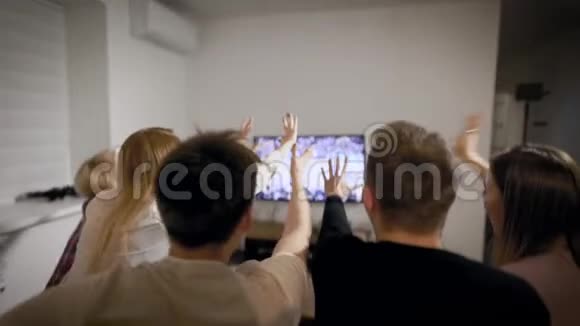 年轻的体育迷们坐在公寓里的沙发上挥舞着双手看电视上的篮球比赛视频的预览图