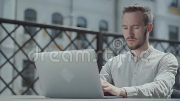 大胡子的年轻人坐在笔记本电脑前的露台上的桌子旁工作自由职业远距离工作的概念视频的预览图