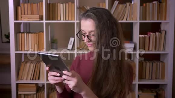 戴眼镜的年轻白种人女学生的特写照片她用平板电脑微笑着看着室内的摄像机视频的预览图