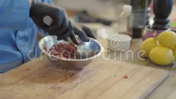 专业厨师用黑色橡胶手套将切碎的肉与调料和油混合在铝碗中视频的预览图