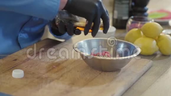 专业厨师的双手戴着黑色橡胶手套将油从铝碗中倒入切碎的肉视频的预览图