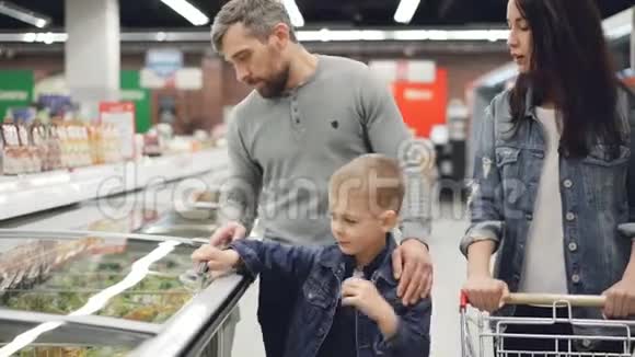 现代家庭在超市里买预先煮熟的冷冻食品男孩打开冰箱拿着袋子他的父母视频的预览图
