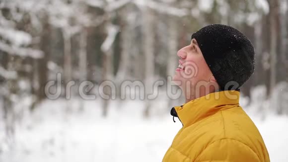 一个穿着黄色夹克衫的人看着树林里冬天的雪慢悠悠地笑着视频的预览图