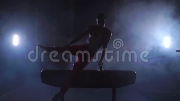 男子体操运动员在黑暗背景下在鞍马上做倒立和旋转动作并在慢动作中吸烟视频的预览图