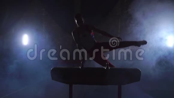 男子体操运动员在黑暗背景下在鞍马上做倒立和旋转动作并在慢动作中吸烟视频的预览图