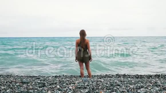小女孩沿着岩石海岸散步有波浪那个女孩长发被风吹起视频的预览图