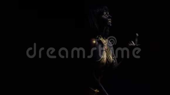 在黑暗中用黑色和金色的化妆和身体艺术跳舞的年轻女人4K视频的预览图