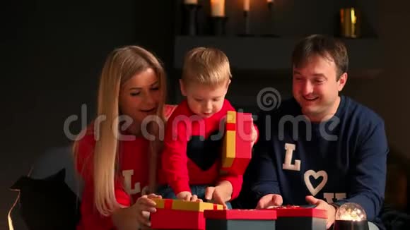 圣诞快乐假期快乐可爱的孩子和父母打开礼物穿睡衣的男孩在附近玩视频的预览图