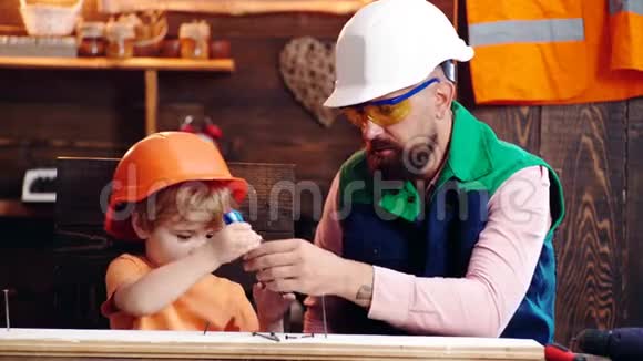 父亲带胡须的家长教小儿子使用工具螺丝刀孩子忙着戴防护头盔的孩子视频的预览图