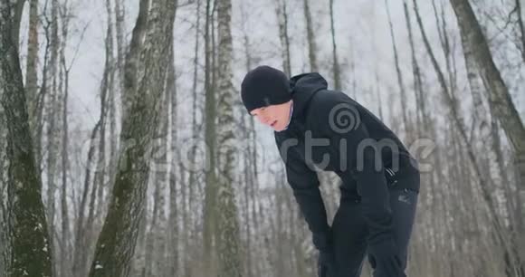 一个年轻人在冬天的森林里晨跑累了停下来喘口气他恢复了体力视频的预览图