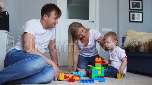 幸福的家庭爸爸妈妈和宝宝在他们明亮的客厅里玩乐高慢镜头拍摄幸福家庭视频的预览图