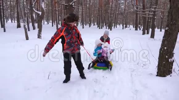 爸爸把婴儿和妈妈卷在雪碟上在冬天的雪林里奔跑笑有女儿的男人和女人视频的预览图