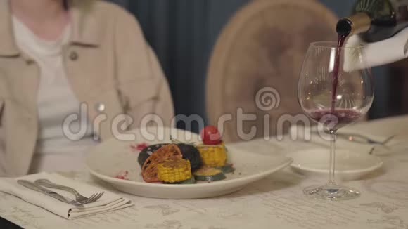 服务员把红酒倒在杯子里让女游客靠近有玉米西葫芦番茄的肉切片视频的预览图