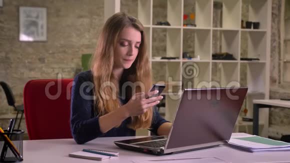 在办公室的笔记本电脑前细心的白种人女商人的肖像在手机上认真地交谈视频的预览图