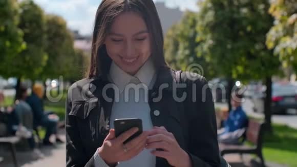 迷人的年轻女子在阳光明媚的城市街头散步和朋友聊天快乐的时髦女孩用手机视频的预览图