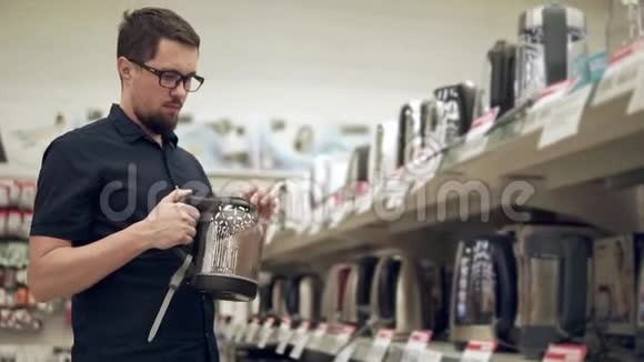 一个留胡子的男人正在五金店的大厅里检查玻璃电水壶视频的预览图