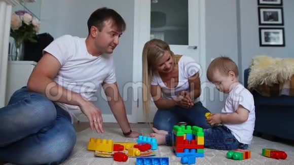 幸福的家庭爸爸妈妈和宝宝在他们明亮的客厅里玩乐高慢镜头拍摄幸福家庭视频的预览图
