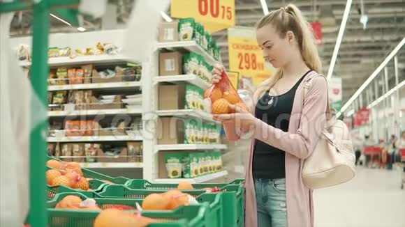 年轻的金发女郎正在超市里拿着带橘子的包裹视频的预览图