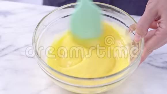 将蛋黄混合到雪纺蛋糕面糊中用绿色硅胶刮刀搅拌工具搅拌直到在玻璃桶中很好地混合视频的预览图