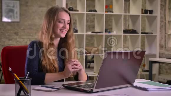 一幅金发美女迷人的白种人女商人在办公室里用笔记本电脑在电视上愉快地交谈的肖像视频的预览图