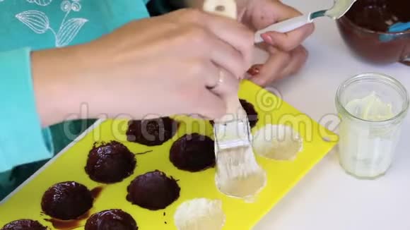 一个女人涂了一种硅胶模具用融化的白巧克力做糖果附近有杏仁作为填充物视频的预览图