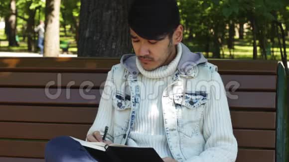 男作家坐在公园里在笔记本上写东西视频的预览图