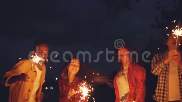 男人和女人用燃烧的火花在户外跳舞和跳跃玩得开心庆祝节日和视频的预览图
