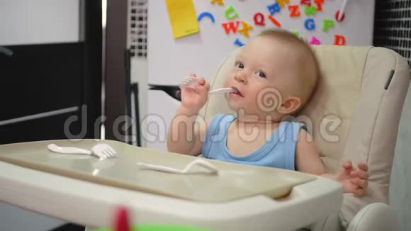 微笑的婴儿在厨房吃食物婴儿坐在高椅子上厨房里有勺子和盘子快乐孩子的画像视频的预览图