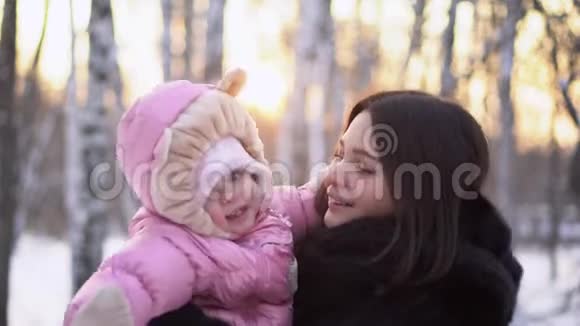 在冬天的户外为年轻快乐的母亲和快乐的孩子做特写穿着粉色连衣裙的小女孩在妈妈手微笑视频的预览图