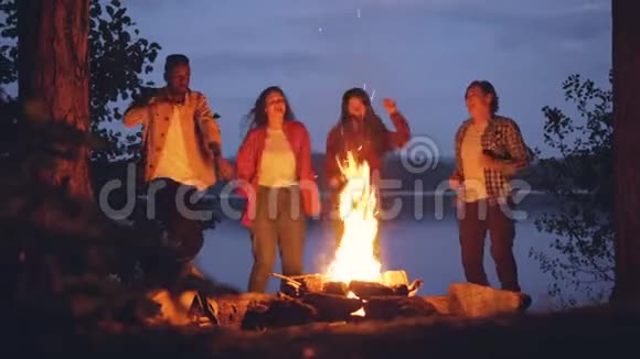 令人兴奋的年轻男女嬉皮士们在明亮的篝火旁跳舞在森林里举行户外聚会玩得开心视频的预览图