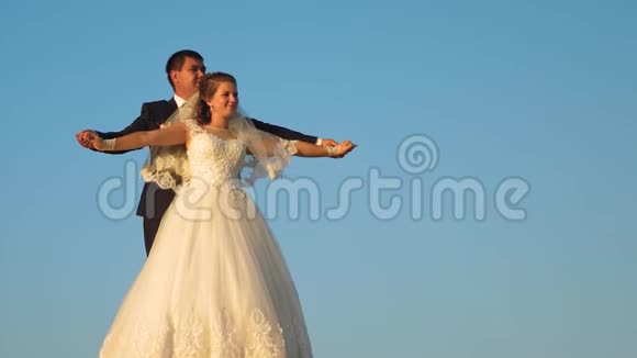 幸福的新娘和新郎穿着白色连衣裙在蓝天上空盘旋微笑着视频的预览图