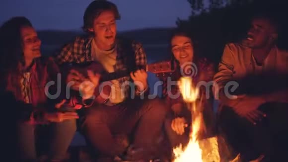 年轻的男人和女人正在唱着吉他的歌在篝火旁休息享受着音乐良好的陪伴视频的预览图