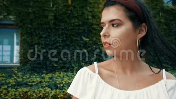 美丽的黑发在树叶中的房子的背景上摆姿势和微笑在西班牙度假戴耳环的女孩视频的预览图