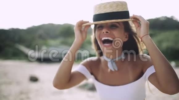 戴着帽子的女孩带着美丽的微笑在海滩上笑视频的预览图