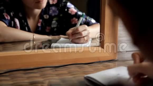 一个年轻的女孩坐在镜子前在我爱你和数字的笔记本上记笔记视频的预览图