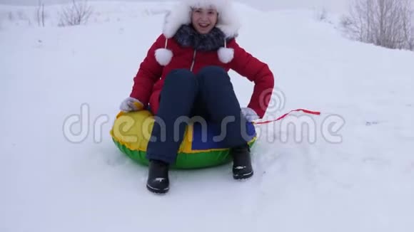 雪盘上的女孩从高高的雪山上滚下来高兴地笑了起来青少年在冬天玩雪橇视频的预览图